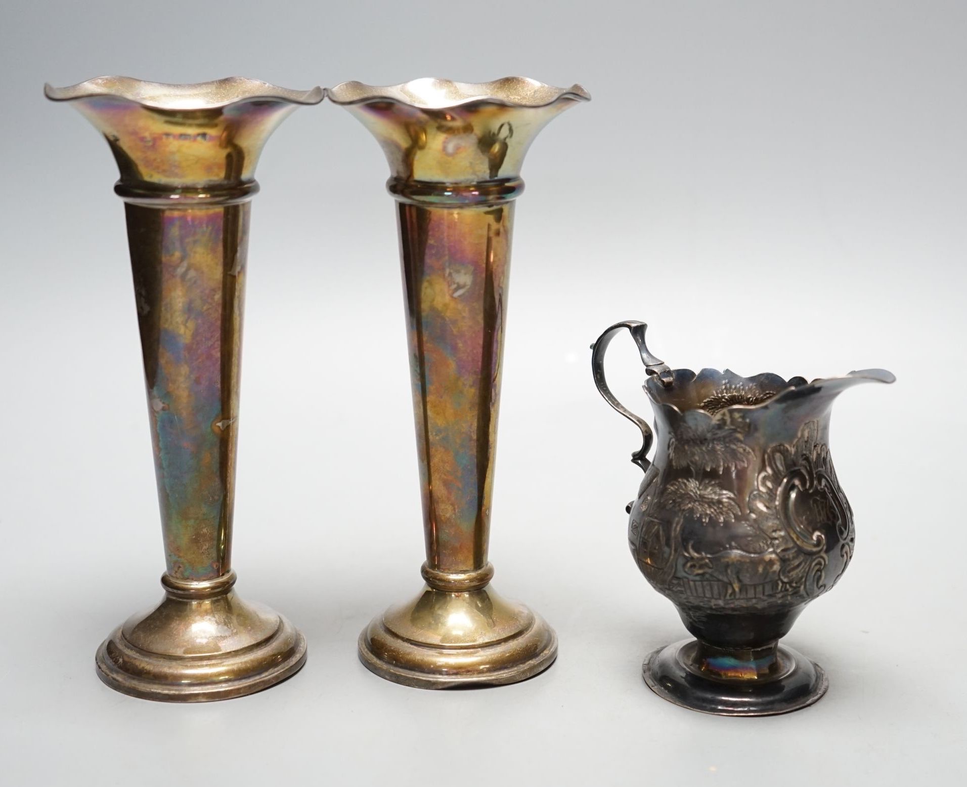 A George III silver helmet shaped cream jug, with later embossed decoration, London, 1759, 97mm and a pair of Edwardian silver spill vases, 16.3cm.